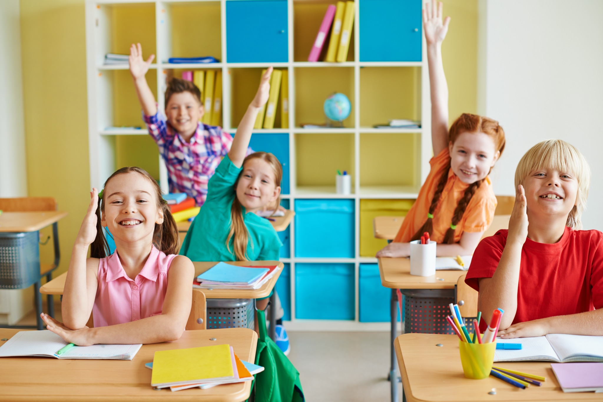 Vrolijke kinderen steken hun hand op in de klas